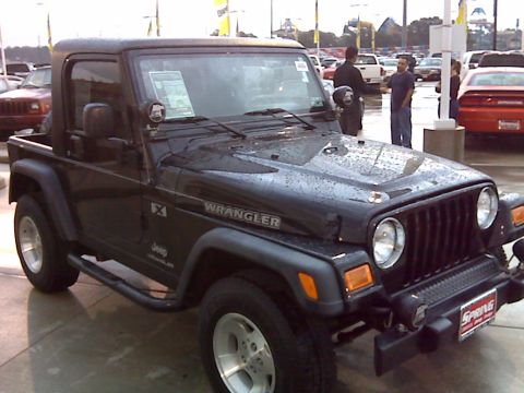 2008 Jeep Wrangler - A black Jeep Wrangler is parked outdoors, possibly at a dealership, with a red Dodge Challenger visible in the background. The Jeep has a h…
