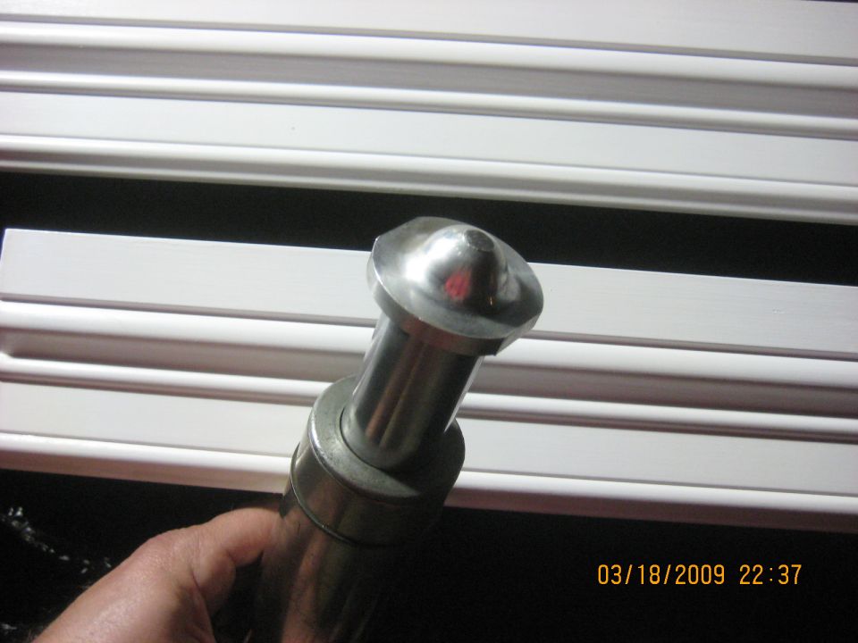 Close-up of a metal part with a rounded top, held by a hand, in front of white trim. Timestamp visible.