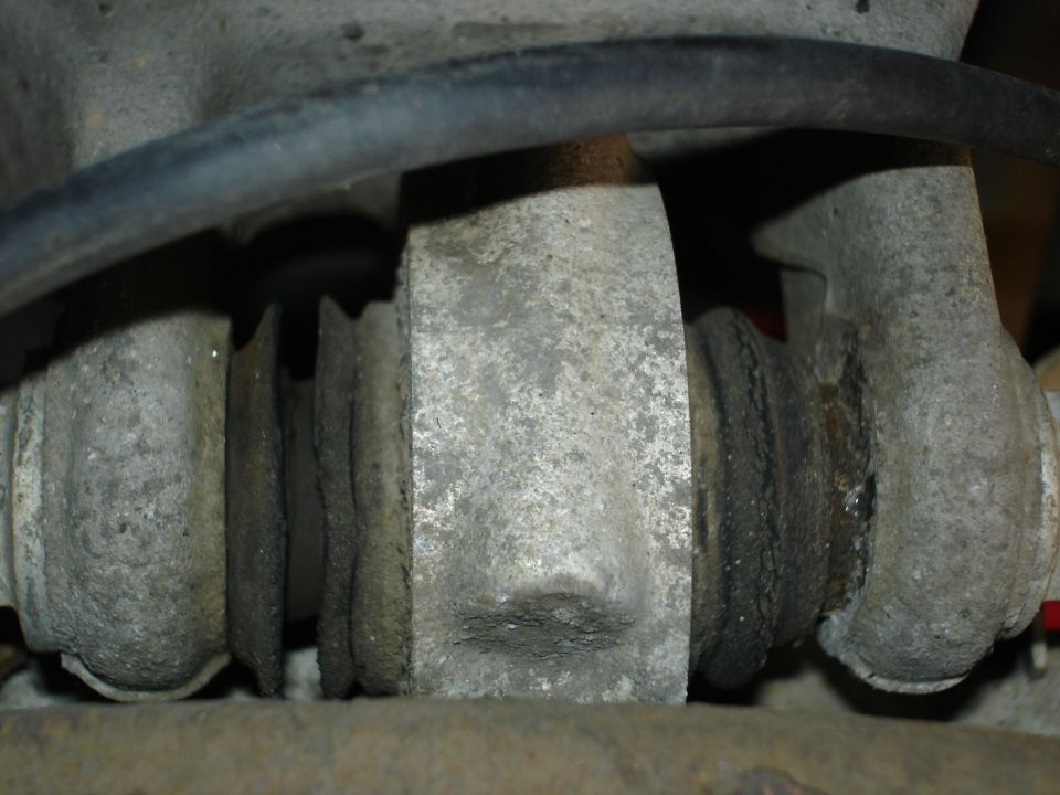 Close-up of dusty suspension joint with rubber bushings and a hose overhead