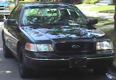 1998 Ford Crown Victoria - A black 1998 Ford Crown Victoria is parked on a street, seen from the front.