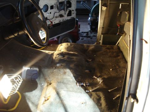 1991 Ford Bronco - The interior of a vehicle is shown with the driver's side steering wheel and dashboard visible. The floor is covered in dark carpet and too…