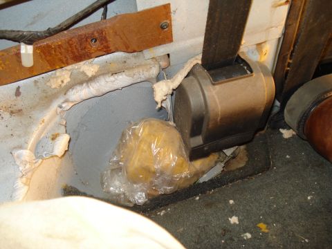 1991 Ford Bronco - A close-up view of a seatbelt retractor mechanism and a yellow object wrapped in plastic, tucked into the floor area of a vehicle. The surr…