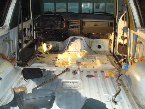 1991 Ford Bronco - Interior view of a dismantled 1991 Ford Bronco, showing the bare floor, dashboard, and steering wheel. Tools and a portable work light are…