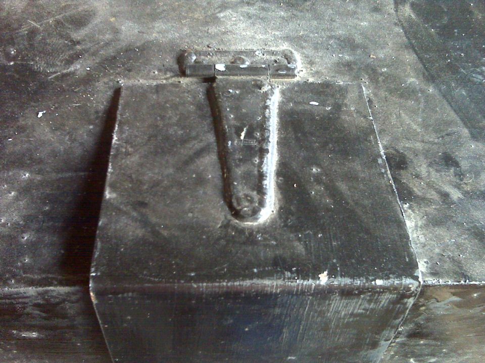 Close-up of a black metal hinge on a dark, textured surface.