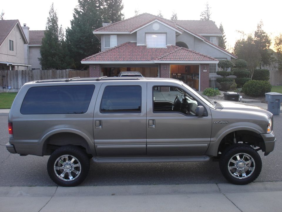 Lifted tan Ford Excursion SUV on chrome wheels, side view, parked on a suburban street