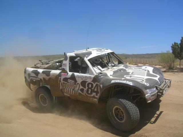 Off-road racing truck with cow print, number 84, driving on dirt.