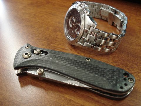 2000 Ford Crown Victoria - A folding knife with a carbon fiber handle and a stainless steel watch with a tachymeter bezel are displayed on a wooden table.