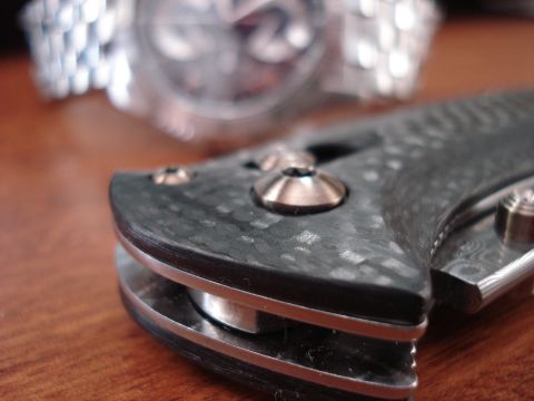 2000 Ford Crown Victoria - A folding knife with a carbon fiber handle is placed next to a wristwatch on a wooden surface.