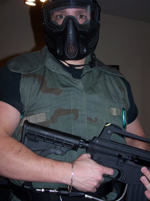 1986 Ford Bronco - A person wearing a black paintball mask and tactical vest holds a black paintball gun. The person has a gold chain bracelet on their left w…