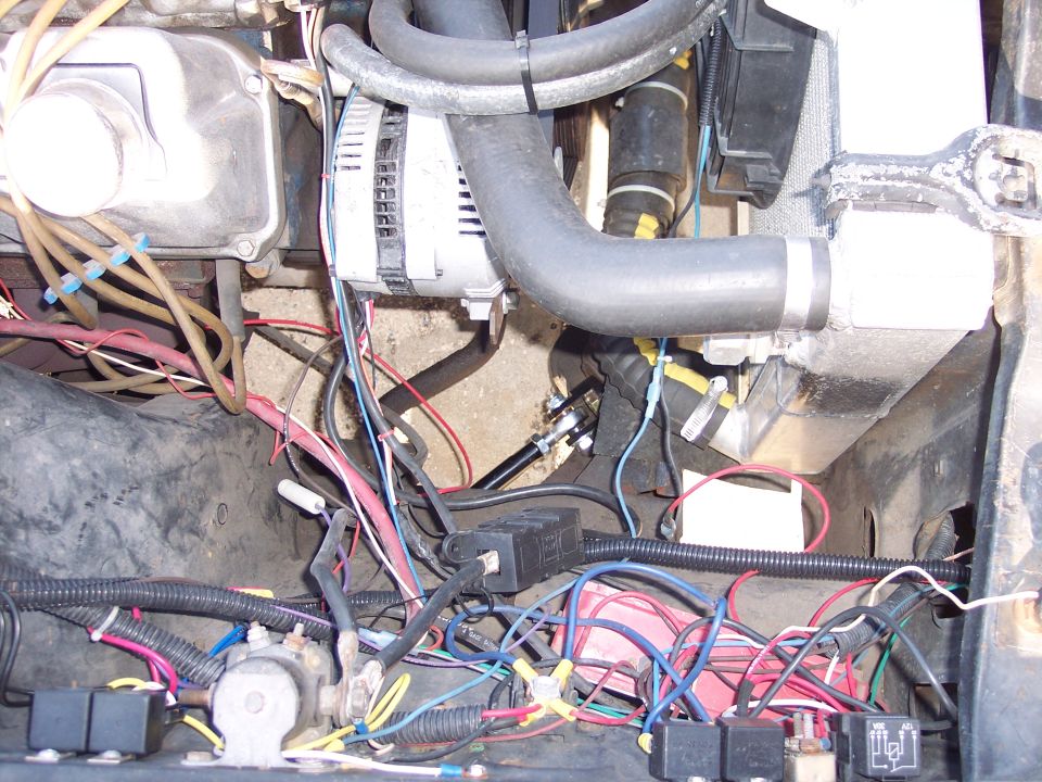 Engine bay of a 1971 Ford Mustang with alternator, hoses, and wiring.