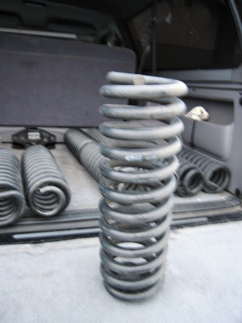 1986 Ford Bronco - Several heavy-duty coil springs are laid out in the cargo area of an SUV. One large spring is prominently displayed in the foreground, with…