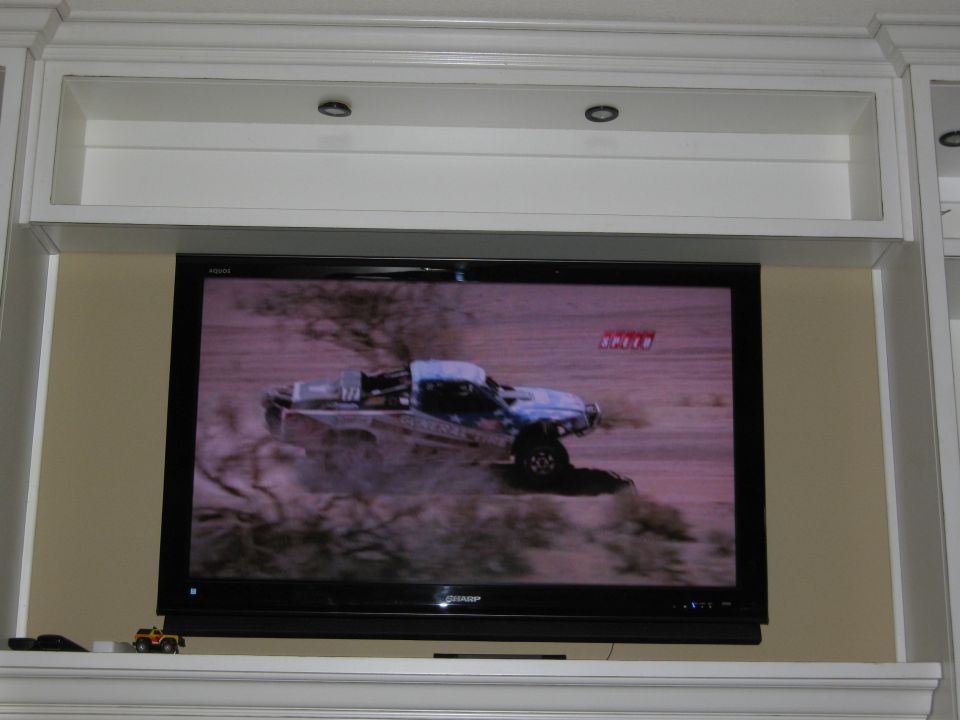 Television screen showing a racing truck, with a toy truck on the shelf below.