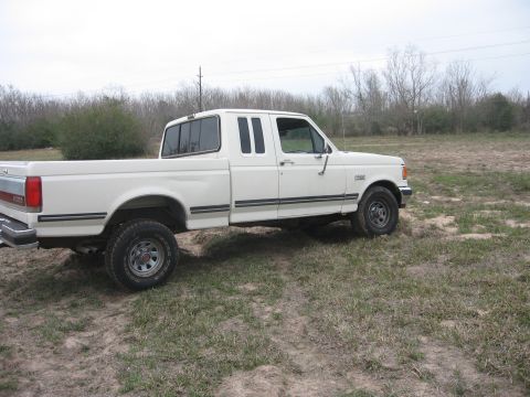 1990 Ford F-150 - A white Ford F-150 pickup truck is parked on a dirt lot with sparse grass and trees in the background. The truck is viewed from the side, s…