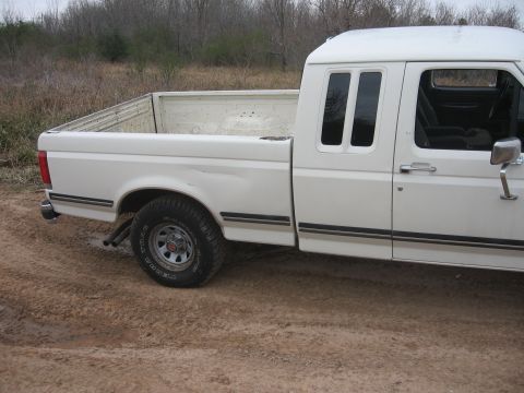 1990 Ford F-150 - The right side of a white Ford pickup truck is shown parked on a dirt road with dry brush in the background. The truck has a standard bed a…