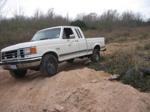 1990 Ford F-150 - A white 1990 Ford F-150 pickup truck is parked on a dirt path with a wooded area in the background. The truck is viewed from a three-quarte…