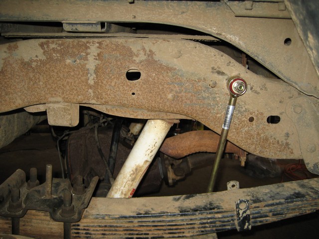 Rusty vehicle undercarriage with sway bar end link and leaf spring.