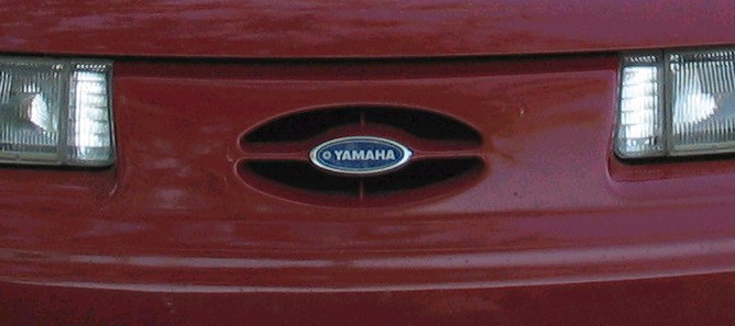Red car grille with oval Yamaha emblem and horizontal bars. Headlights visible on sides