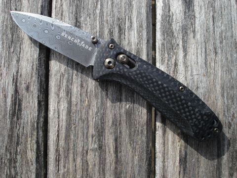2000 Ford Crown Victoria - A close-up shot of a Benchmade folding knife with a Damascus steel blade and a carbon fiber handle rests on a weathered wooden surface.