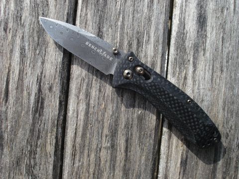 2000 Ford Crown Victoria - A folding knife with a Damascus steel blade and a carbon fiber handle rests on a weathered wooden surface.