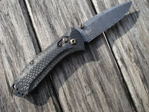2000 Ford Crown Victoria - A folding knife with a Damascus steel blade and a carbon fiber handle rests on a weathered wooden surface.