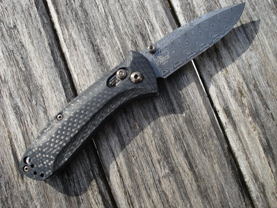 Folding knife with Damascus blade and carbon fiber handle on wood