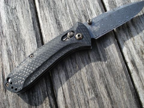2000 Ford Crown Victoria - A close-up view of a folding knife with a Damascus steel blade and a carbon fiber handle rests on a weathered wooden surface.