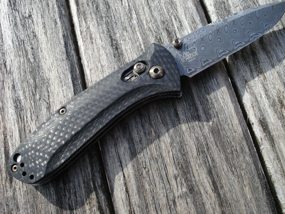 Folding knife with Damascus blade and carbon fiber handle on wood
