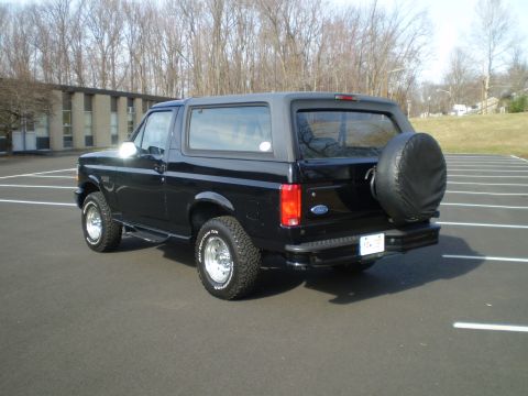 1996 Ford Bronco - The rear passenger side of a black 1996 Ford Bronco is shown parked in a lot. A spare tire is mounted on the rear door, and the vehicle has…