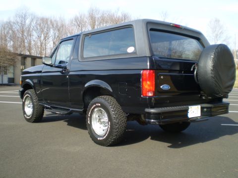 1996 Ford Bronco - The rear passenger side of a black 1996 Ford Bronco is shown parked on asphalt. The vehicle has a spare tire mounted on the back and a lice…