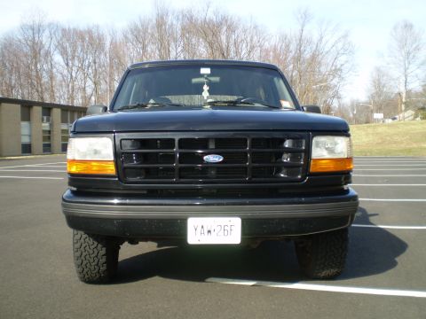 1996 Ford Bronco - The front view of a black 1996 Ford Bronco is parked in a paved lot with white lines. The vehicle has a black grille with a Ford logo and a…