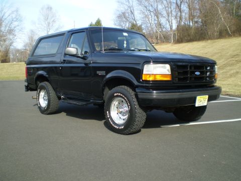 1996 Ford Bronco - A black 1996 Ford Bronco is parked on an asphalt surface with white parking lines. The front passenger side of the SUV is angled towards th…