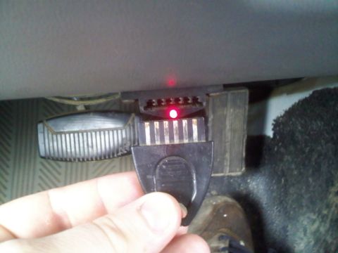 1994 Ford Bronco - A hand holds a black OBD-II scanner with red indicator lights plugged into a vehicle's diagnostic port, located under the dashboard near th…