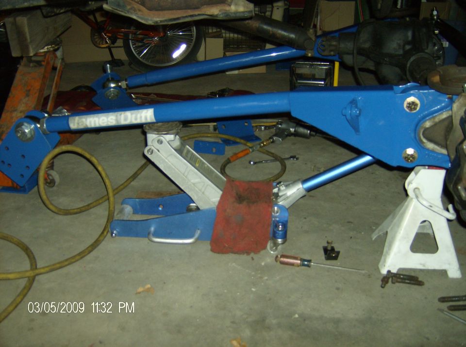 Blue suspension part labeled "James Duff" on a vehicle, supported by jacks.