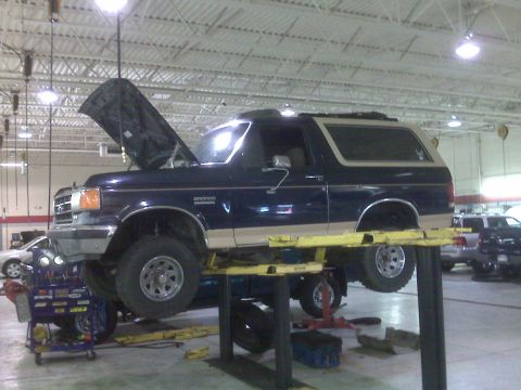 1990 Ford Bronco - 1990 Ford Bronco undergoing service on a hydraulic lift in a garage.