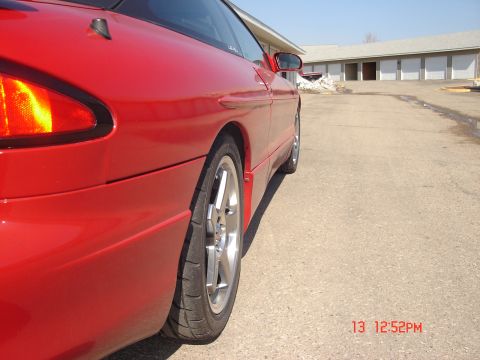1993 Ford Probe - The rear passenger side of a red 1993 Ford Probe is shown from a low angle, focusing on the taillight and wheel. The car is parked on a pav…