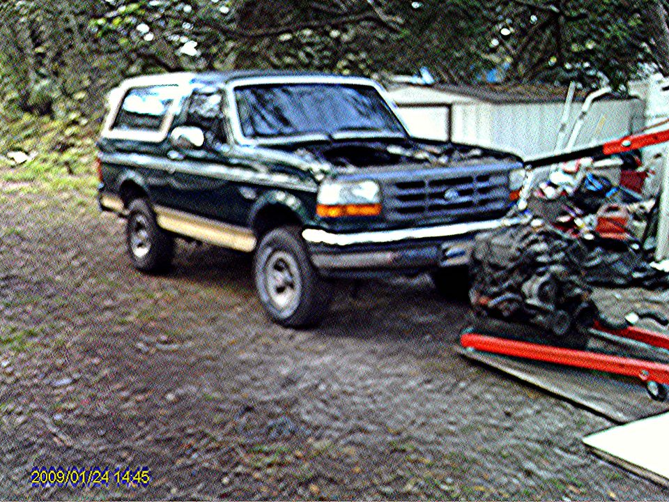 1992 Ford Bronco parked outdoors with an engine on a stand nearby.