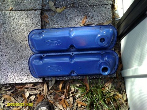 1992 Ford Bronco - Two blue Ford valve covers are shown resting on concrete blocks and dry leaves. The valve covers have the Ford logo embossed on them and on…
