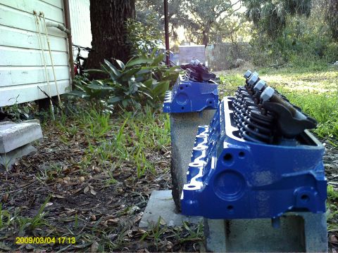 1992 Ford Bronco - Two blue painted Ford V8 engine cylinder heads are placed on concrete blocks outdoors. The cylinder heads are viewed from the side with the…