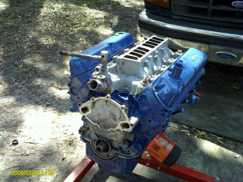 1992 Ford Bronco - A blue Ford V8 engine sits on an engine stand outdoors, in front of a dark-colored Ford truck grille. The engine is partially assembled wit…