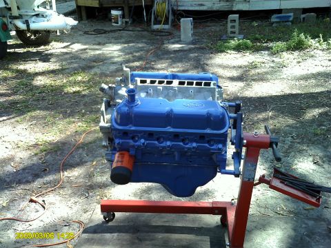 1992 Ford Bronco - A blue Ford V8 engine is mounted on a red engine stand outdoors. The engine has blue valve covers and an orange oil filter is visible.