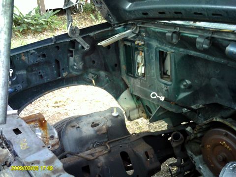 1992 Ford Bronco - The engine bay of a dark green Ford Bronco is shown, with the hood open, revealing the inner fender wells and firewall. Various mechanical…