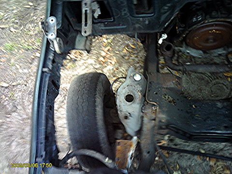 1992 Ford Bronco - The underside of a vehicle, likely a 1992 Ford Bronco, shows a worn tire and exposed engine components. The scene is outdoors with dirt and…