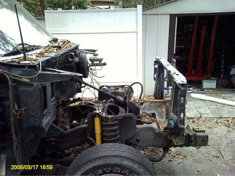 1992 Ford Bronco - The front end of a dark green vehicle, likely a truck or SUV, is shown disassembled. The chassis, engine components, and suspension are vis…