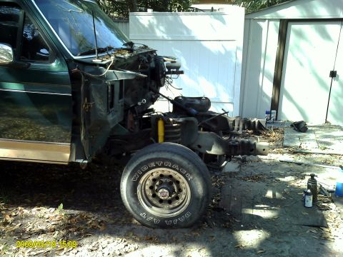 1992 Ford Bronco - The front passenger side of a dark green Ford Bronco is shown, partially disassembled with the front end removed. The vehicle is parked out…