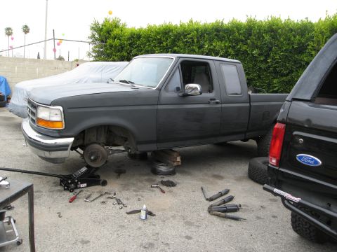 1986 Ford Bronco - A dark gray Ford pickup truck is parked outside with its front wheels removed and the vehicle supported by wooden blocks and a hydraulic ja…