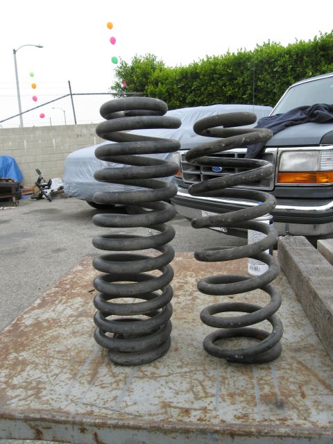 1986 Ford Bronco - Two large black coil springs are displayed on a rusty metal surface in front of a Ford truck. Several colorful balloons float in the sky be…