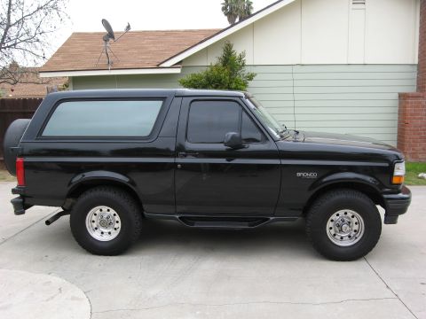1986 Ford Bronco - A black 1980s Ford Bronco is parked on a concrete driveway in front of a house with a satellite dish on the roof. The vehicle is shown in a…