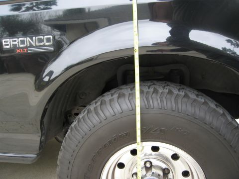 1986 Ford Bronco - A close-up side view shows the front fender and tire of a black Ford Bronco. A yellow measuring tape is positioned vertically along the fen…