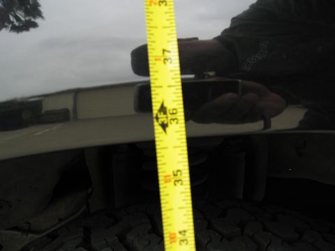 1986 Ford Bronco - A yellow measuring tape is held vertically against the glossy black fender of a vehicle, showing a measurement around 36.5 inches. The refl…