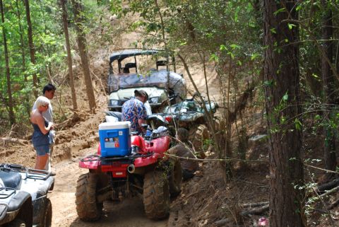 2008 Jeep Wrangler - Several ATVs are parked on a muddy trail in a wooded area, with people gathered around them. One red ATV in the foreground has a blue coole…